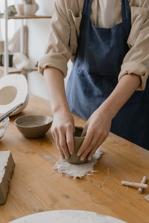 Free Artisan hands shaping clay on a wooden work table in a pottery studio. Stock Photo