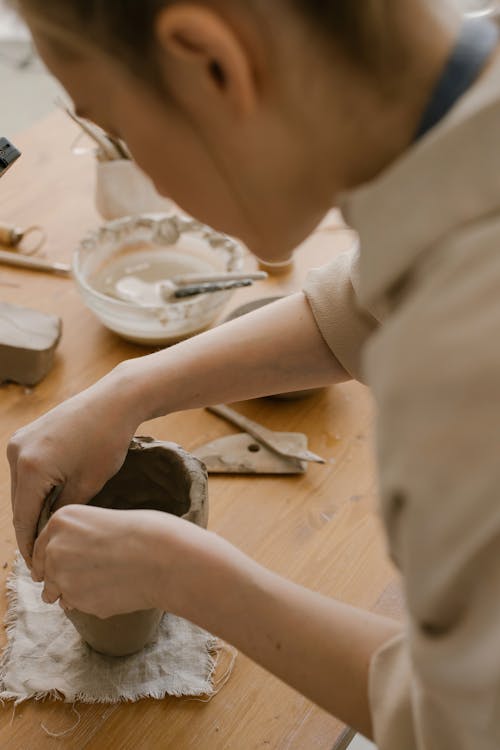 A Woman Shaping a Clay on the Wooden Table