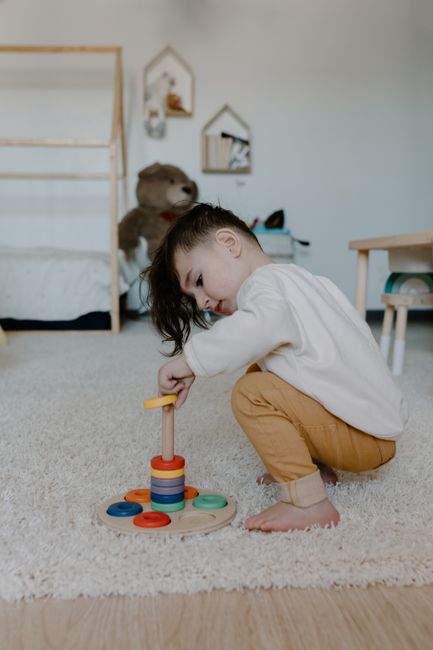 Fotomural Un niño pequeño jugando con un colorido juguete de apilar de madera en el interior, promoviendo el aprendizaje temprano.
