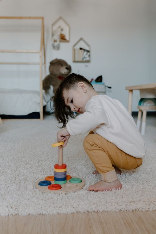 Free A young child playing with a colorful wooden stacking toy indoors, promoting early learning. Stock Photo