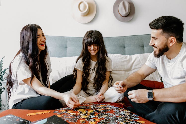 A Family Sitting On Bed Putting The Puzzle Pieces Together