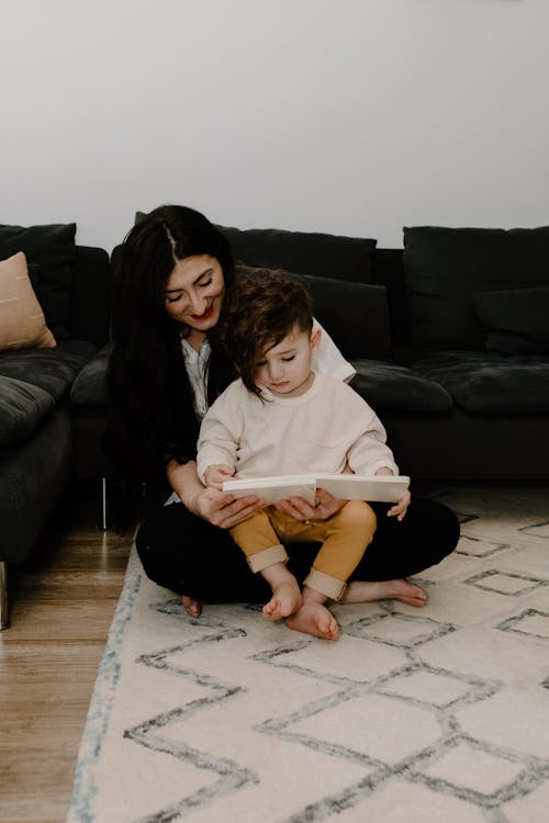 Free A Boy Reading a Book with her Mother while Sitting on the Floor Stock Photo