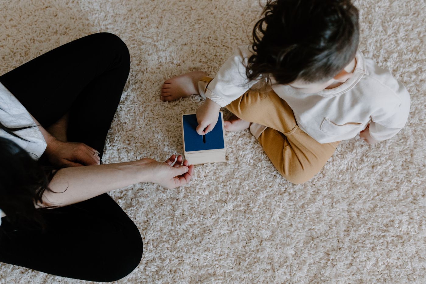 A parent supporting a young child during a hands-on wooden learning activity