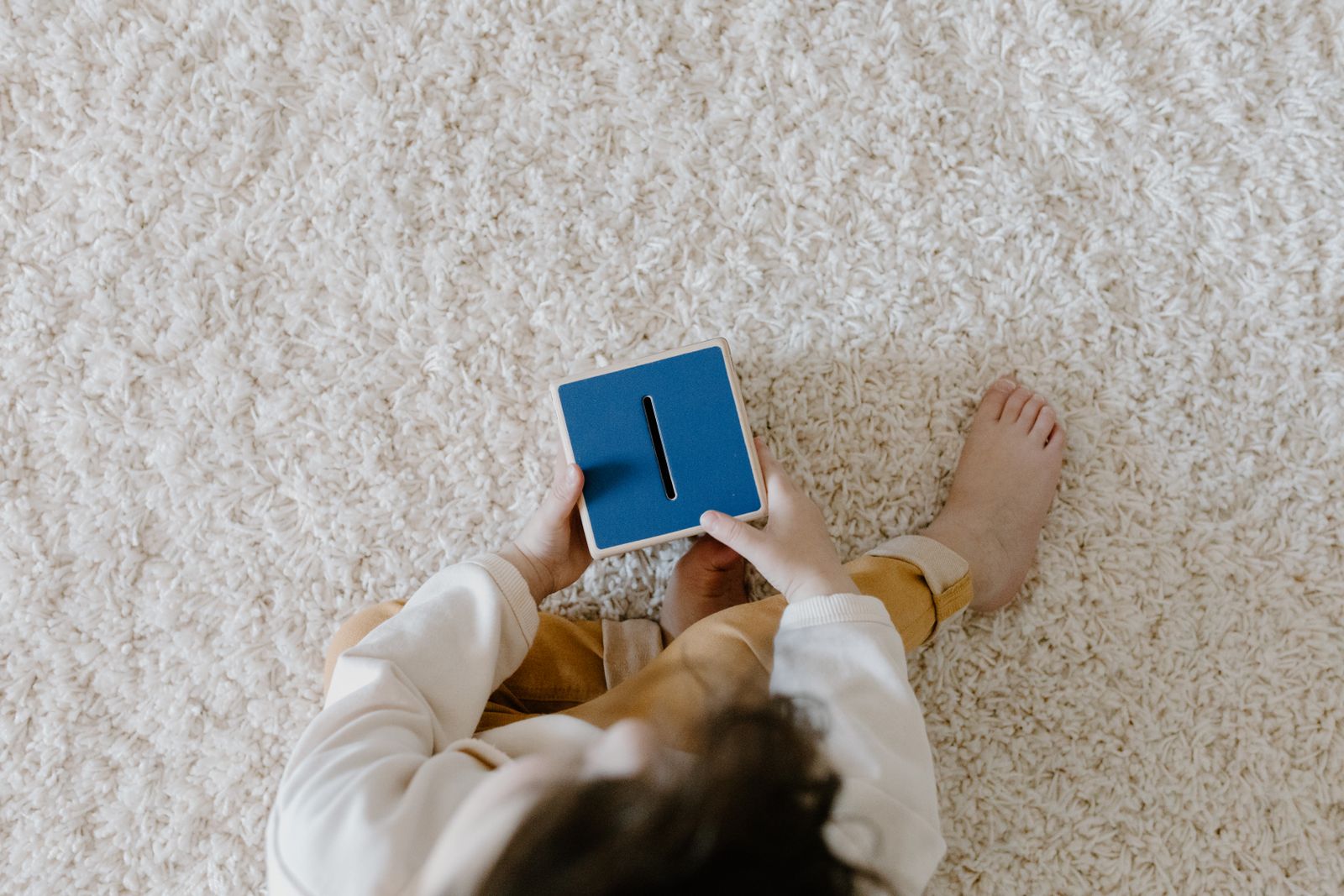 A young child holding a blue piggy bank during a home money learning activity