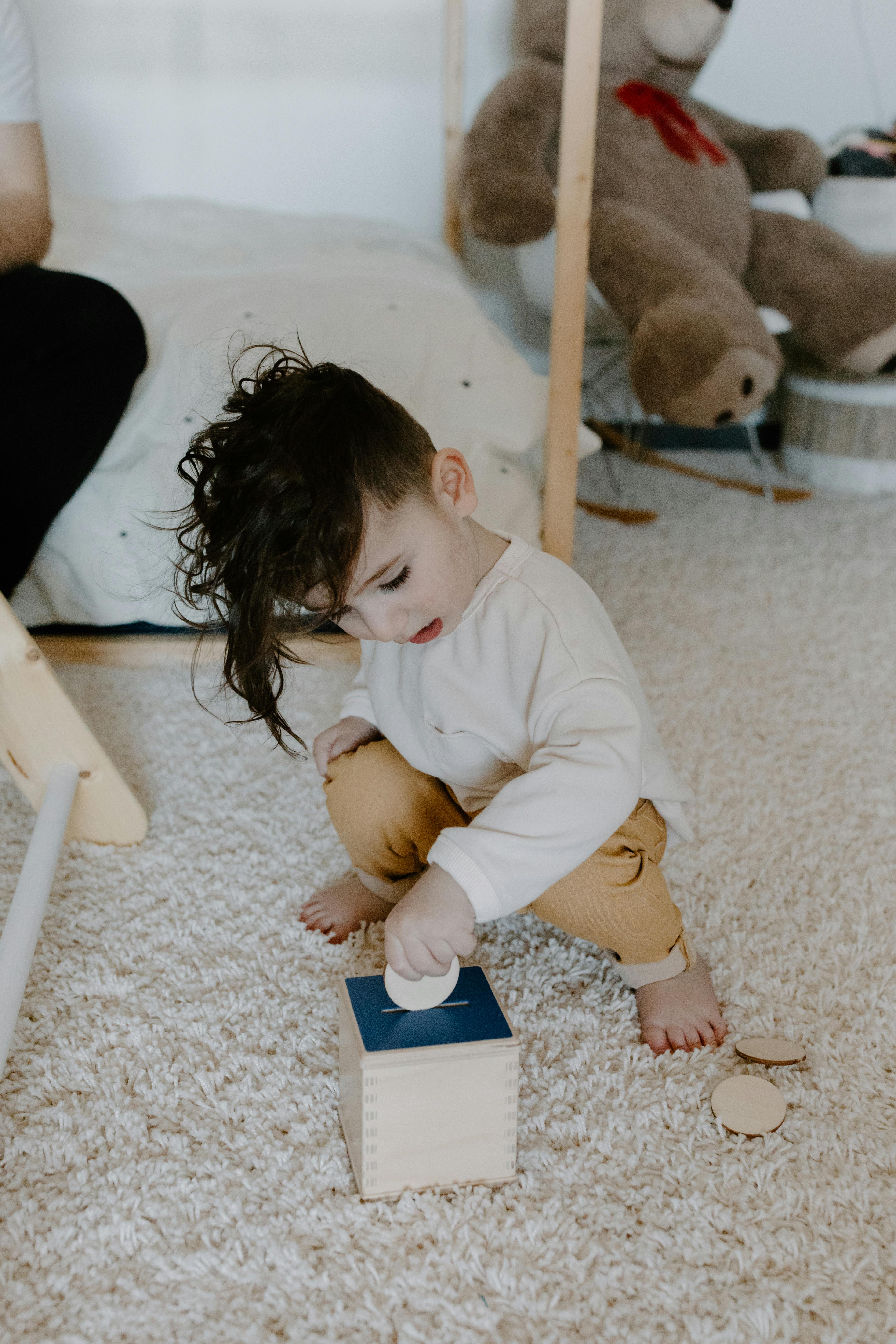 a toddler inserting a coin in a square coin box