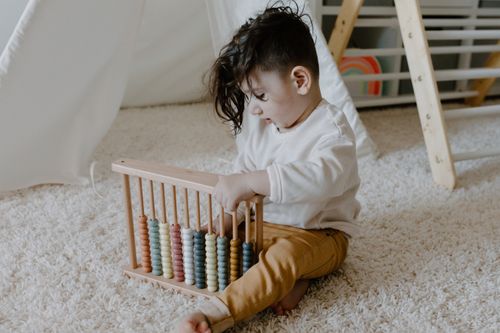 Free Young child sits on a carpet playing with a colorful wooden abacus in a cozy indoor setting. Stock Photo