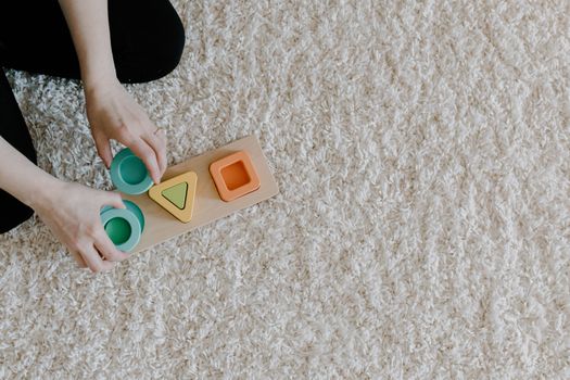 A person arranging a sustainable wooden toy on a carpet, promoting mindful and sustainable learning.