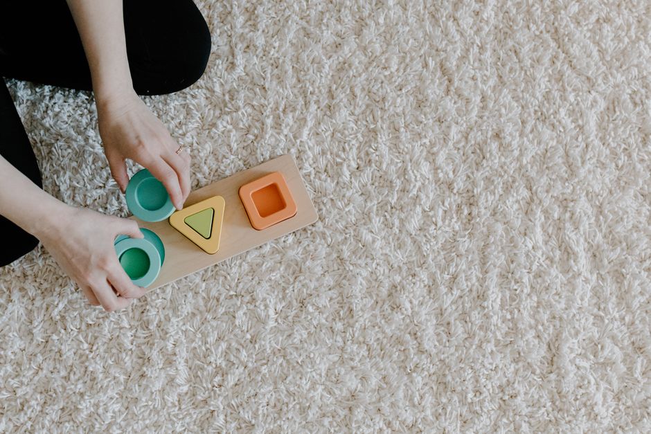 A person arranging a sustainable wooden toy on a carpet, promoting mindful and sustainable learning.