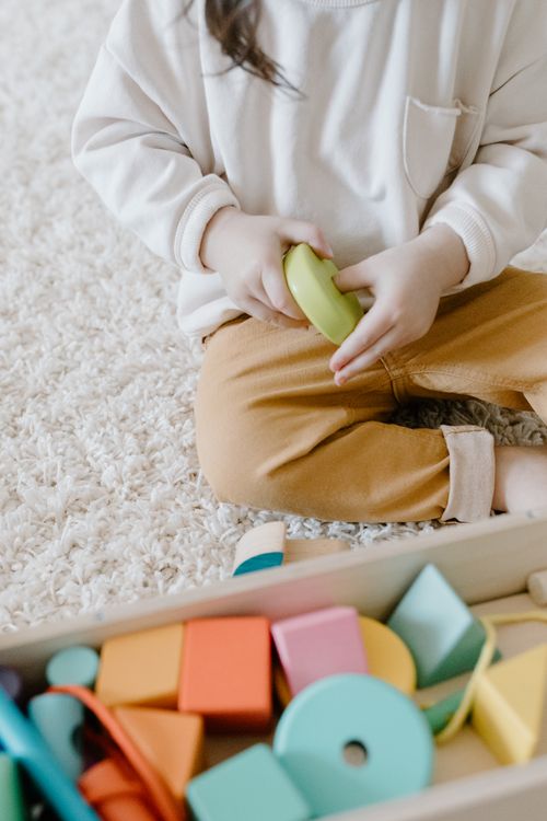 Free Young child sitting on a carpet playing with colorful educational toys indoors. Stock Photo