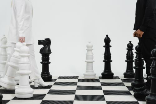 Free Two individuals strategize over a life-sized chess game indoors. Stock Photo