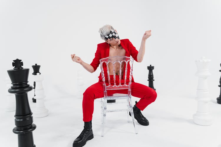 Man In A Red Suit Sitting On The Chair With Chess Pieces