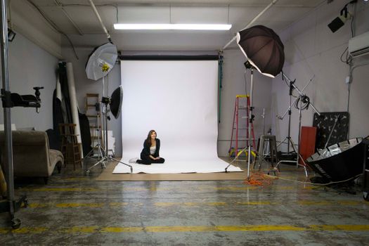 Photography studio featuring a professional setup with lighting equipment and a model sitting on the floor.