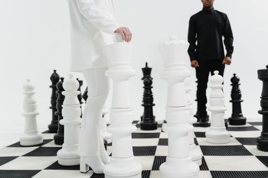A person in a white suit plays on a large indoor chessboard with oversized pieces.