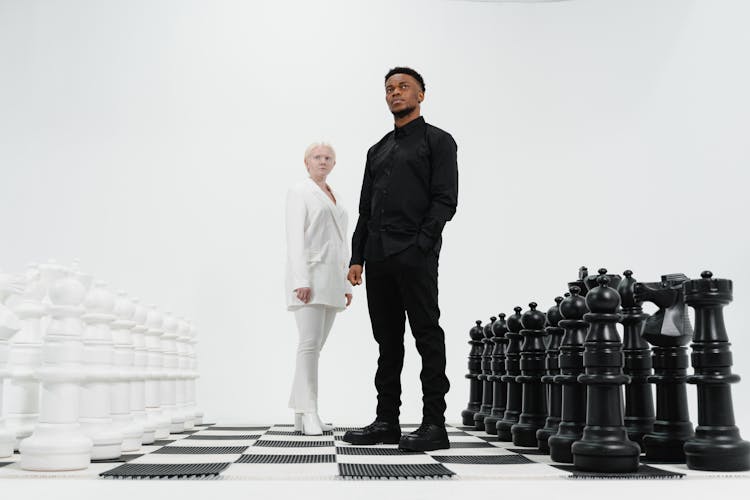 A Man And A Woman Standing On A Giant Chessboard