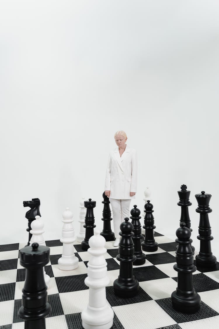 A Person In A White Suit Standing On A Giant Chess Board