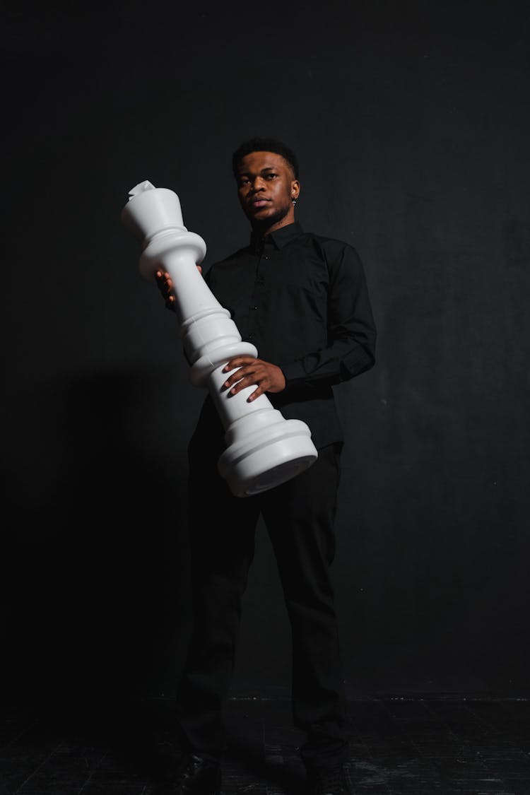 A Man In A Black Outfit Holding A Giant Chess Piece