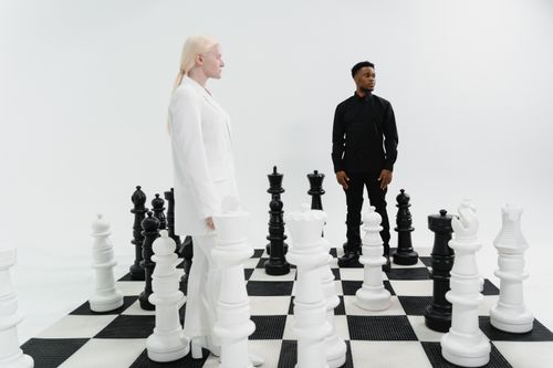 Free Two individuals strategize on a life-size chessboard, immersed in a game of intellect. Stock Photo