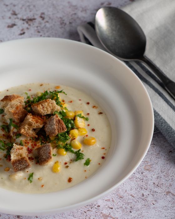 Creamy pale corn soup topped with rye croutons, corn kernels, parsley and chili flakes