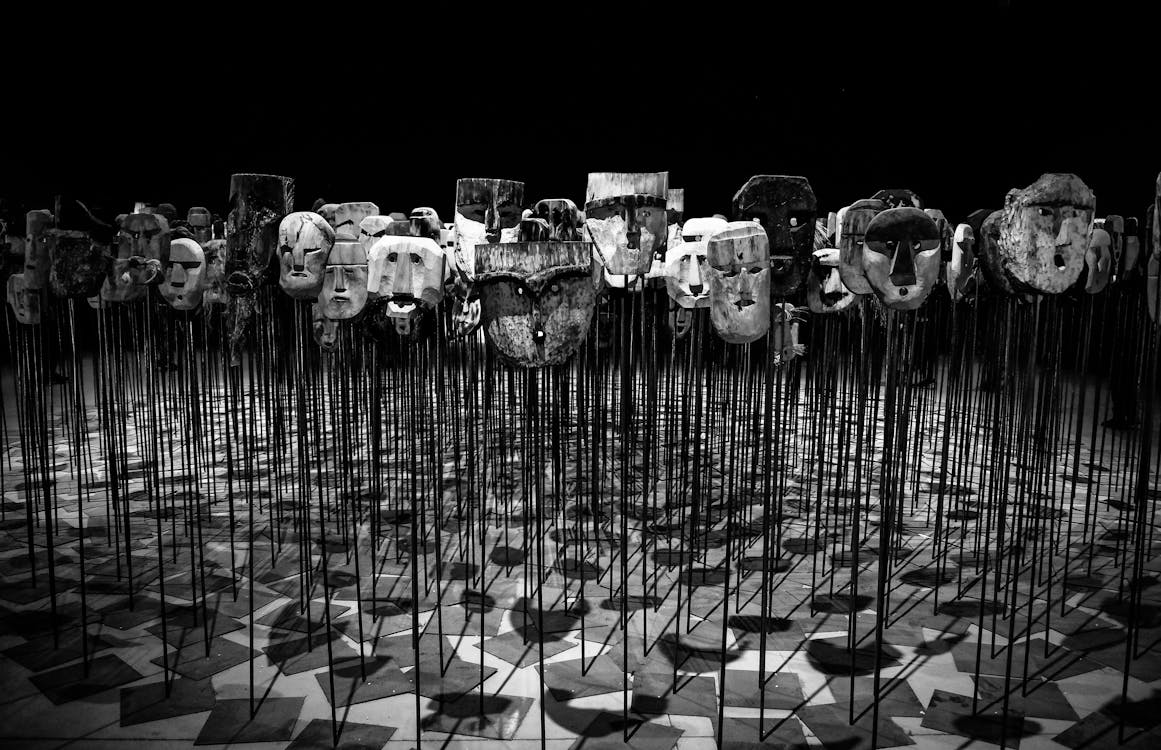 Greyscale Photo of Masks on a Stick