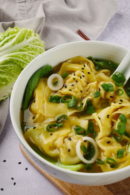 Warm and delicious wonton soup with fresh vegetables garnished with scallions and sesame seeds.