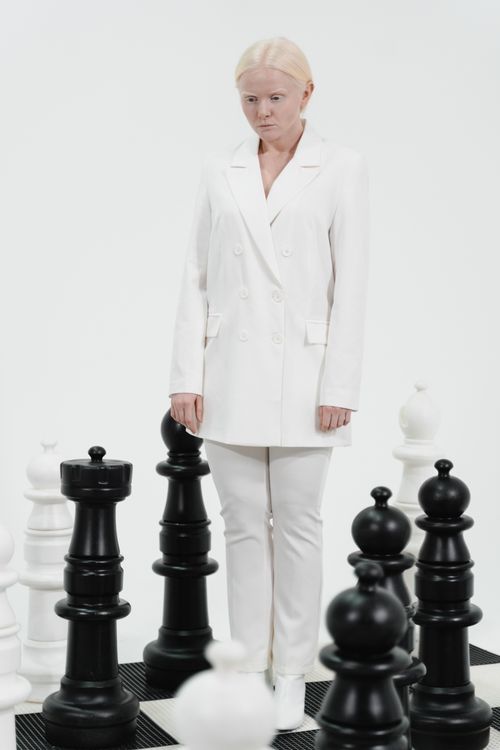 Free A conceptual studio photo of a woman in a white suit surrounded by oversized chess pieces. Stock Photo