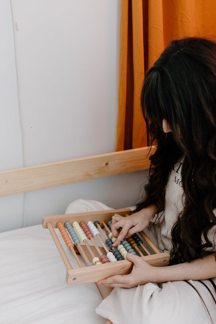 Child Sitting On A Bed Holding An Abacus