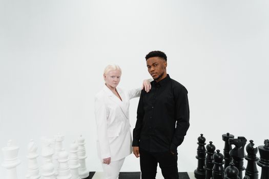 A fashion photoshoot featuring two models in black and white suits posing with large chess pieces.