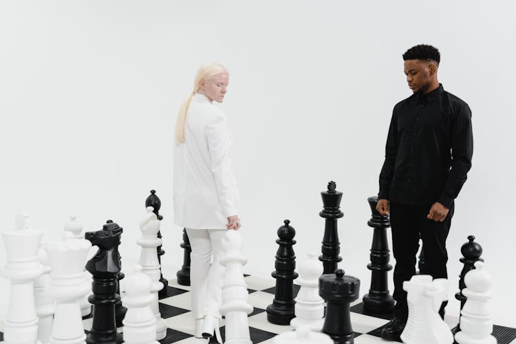 A Woman In White Blazer And A Man In Black Long Sleeves On A Giant Chessboard