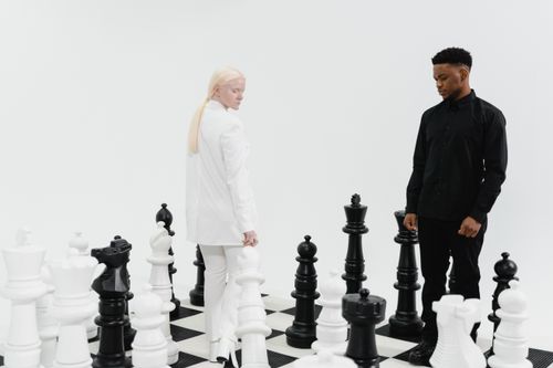 Free Two individuals engage in a strategic chess game with giant pieces on a checkered board. Stock Photo
