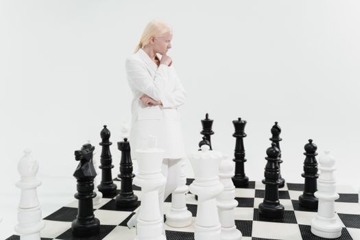 Woman in white suit contemplating large chess pieces on a black and white board.