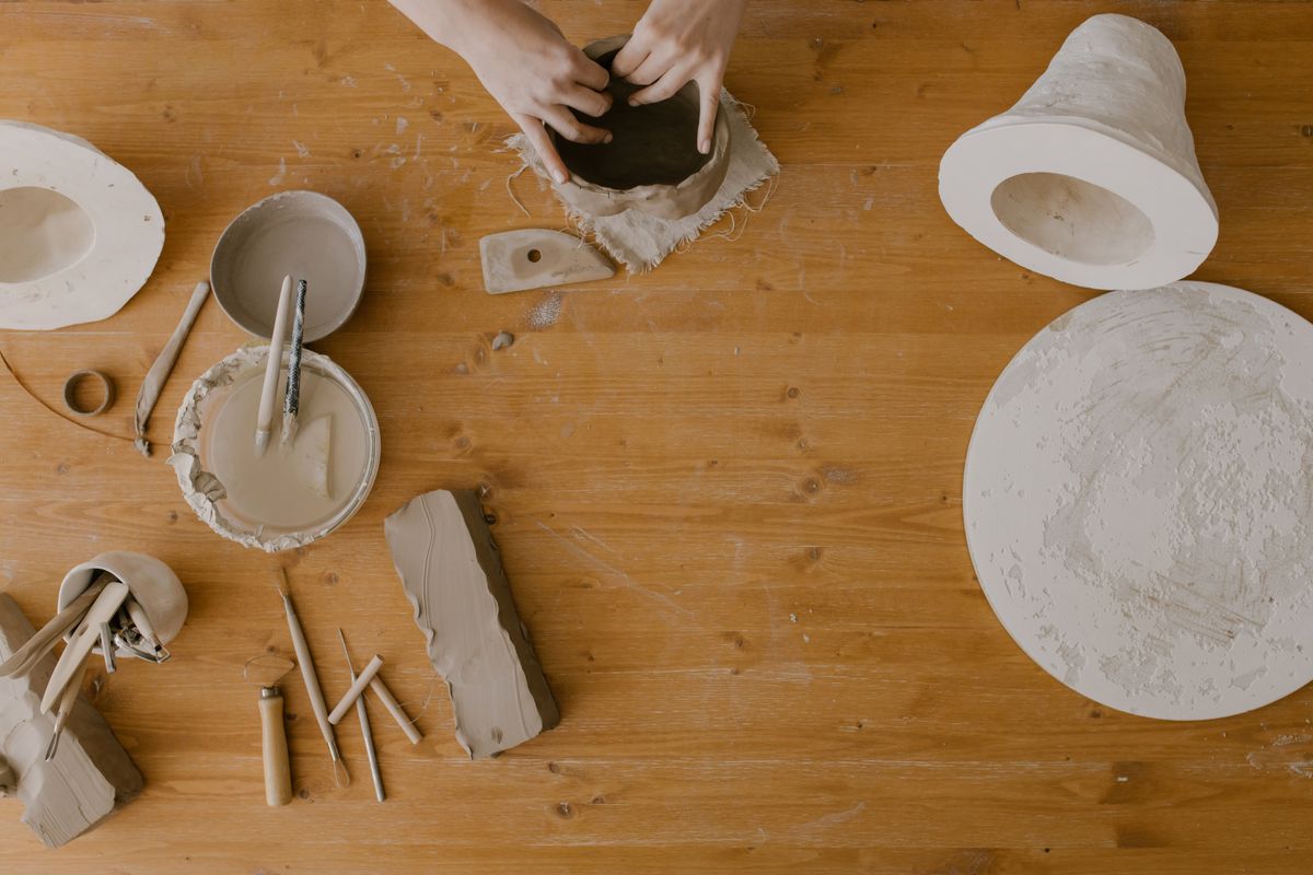 Pottery tools and unfired pieces laid out on a wooden bench. Photo by cottonbro studio on Pexels.