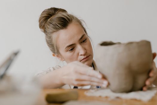 A woman attentively shaping a clay pot in a pottery workshop, showcasing creativity and skill.