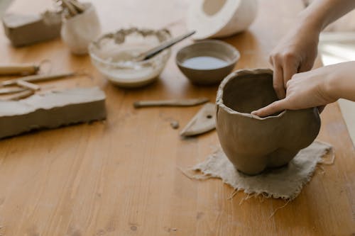 Hands of a Person Molding Clay on a Wooden Table Top