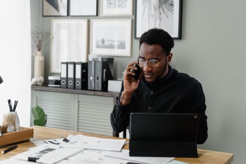Free Professional man working at his desk on a call, managing documents and using a tablet. Stock Photo