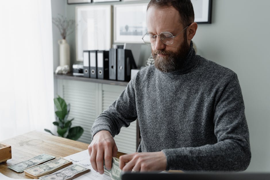 How Ally Buckets Organize Savings Goals Better An adult man in a gray sweater counting dollar bills at a wooden desk, showcasing financial management.