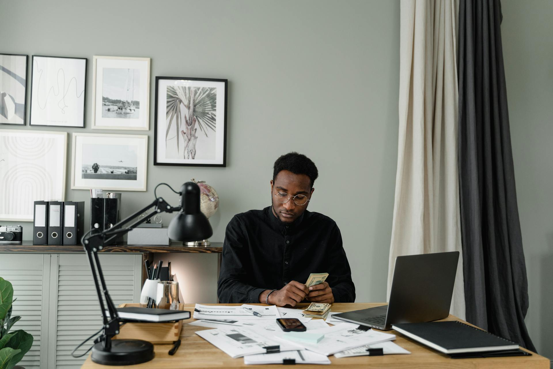 Serious businessman counting money at a desk in a modern office setting.