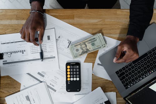 Cash, Computer Laptop, Pen and Paperwork on Wooden Surface