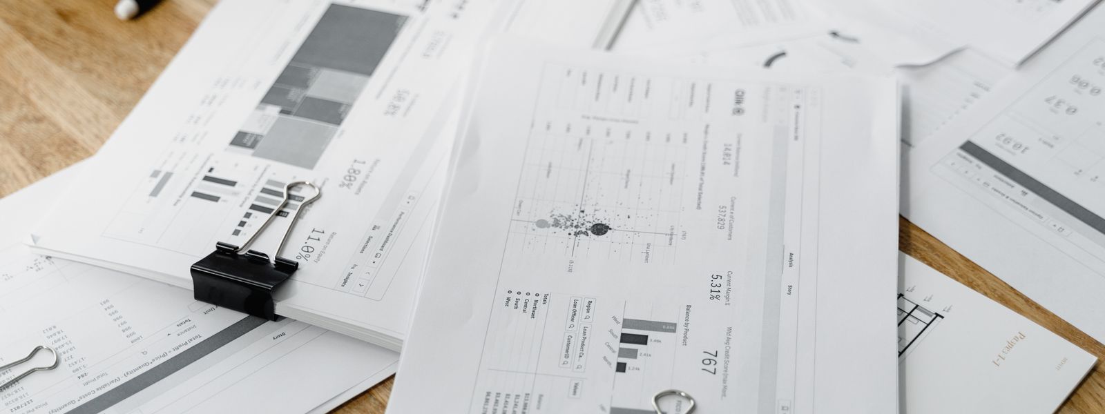 A stack of financial reports and graphs with clips on a wooden desk, highlighting business planning.