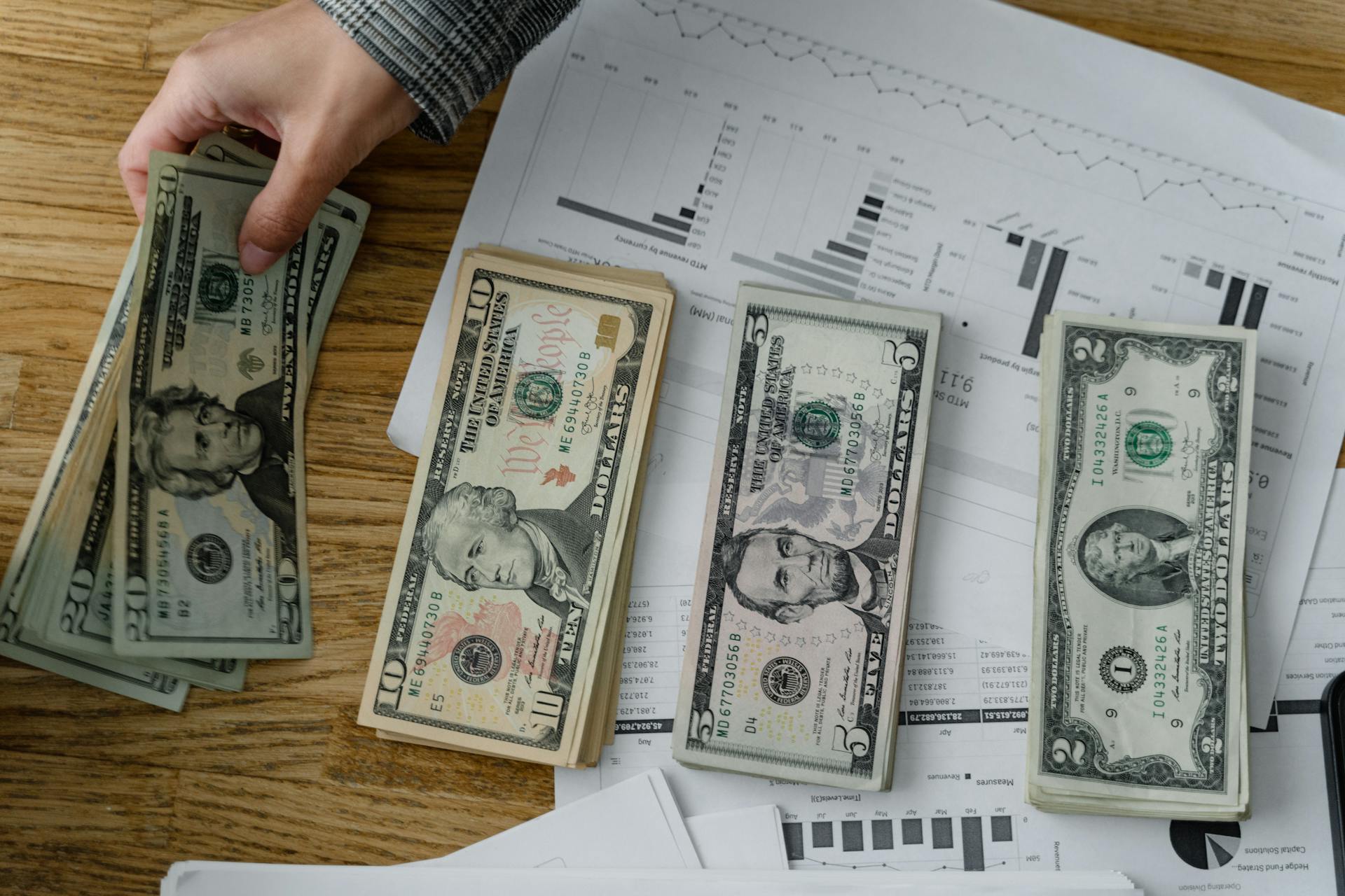 Person holds US dollars over financial papers, showing income or budget analysis.