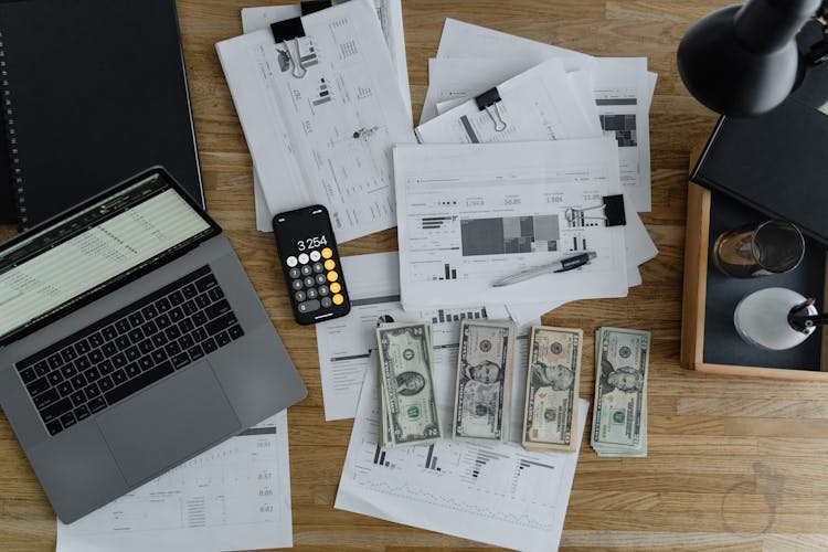 A Laptop Near The Dollars And Papers On A Wooden Table