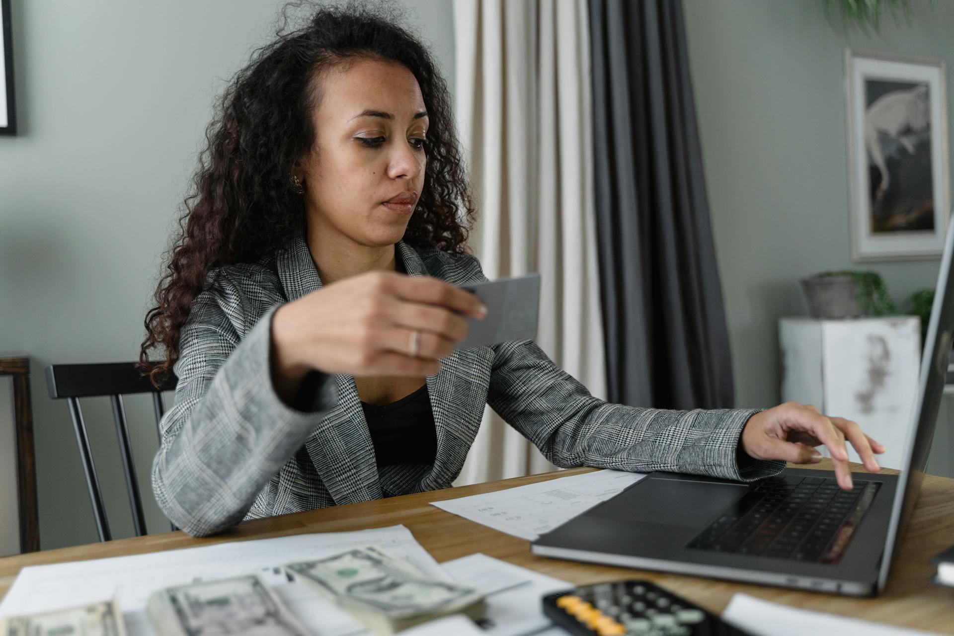 Woman using a laptop and managing finances with cash and card on a wooden table indoors.