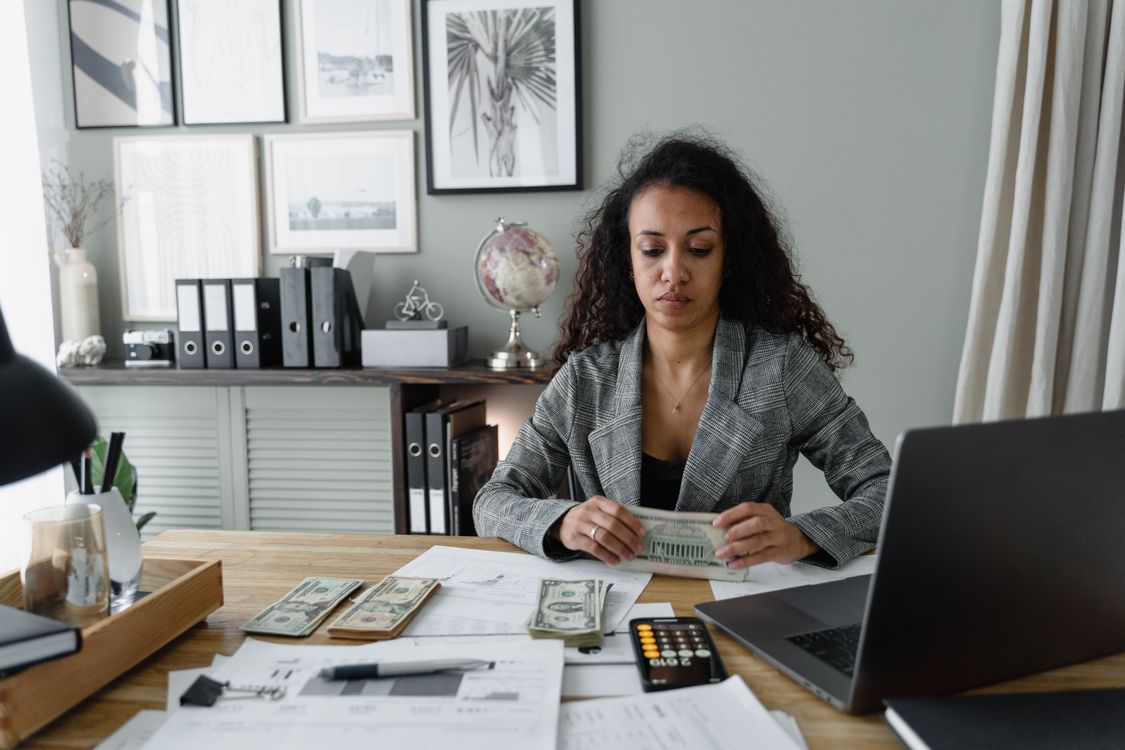 Free Focused woman counts cash at desk surrounded by office items, emphasizing finance and professionalism. Stock Photo