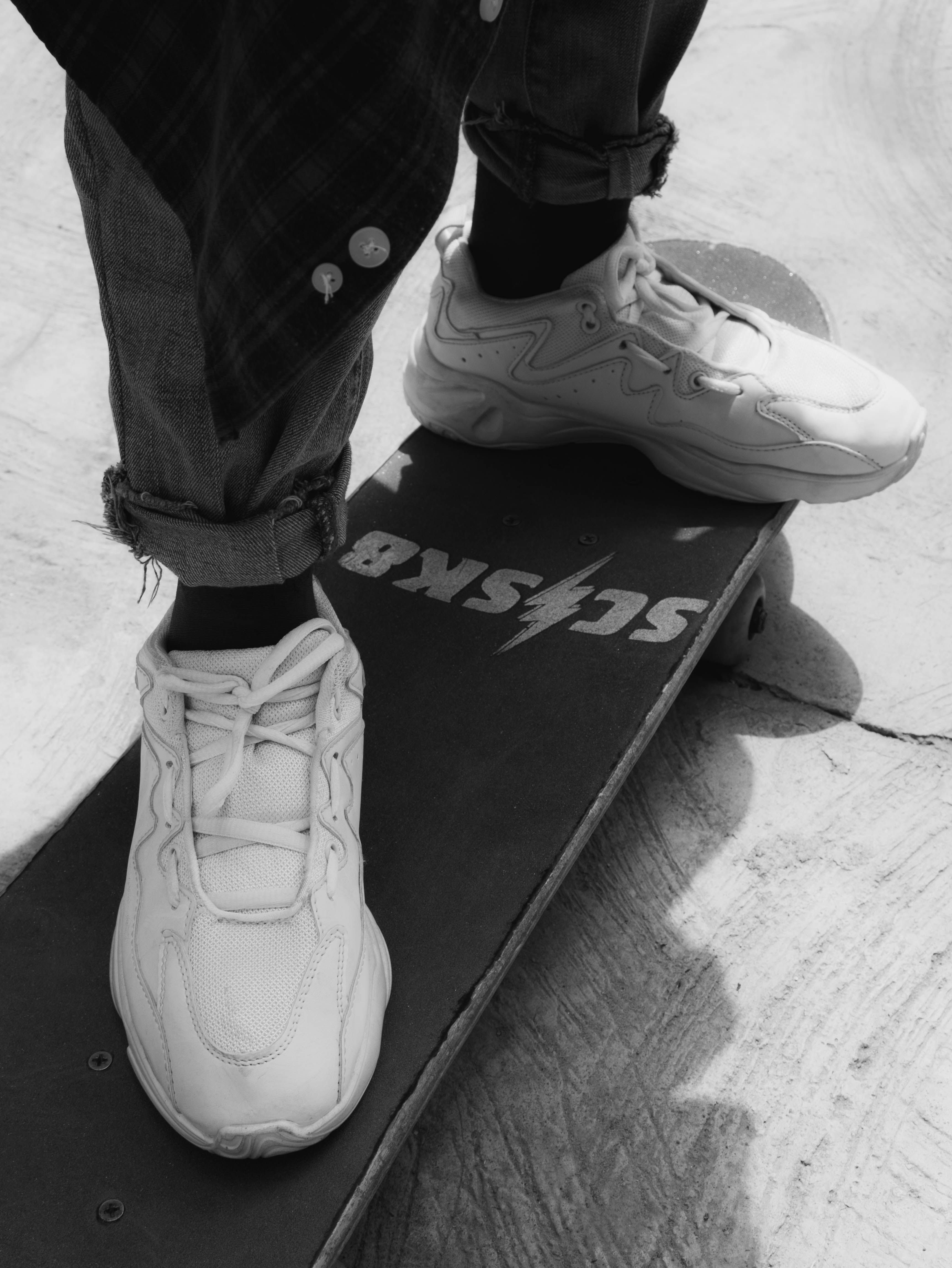Black and white image of sneakers standing on a skateboard deck.