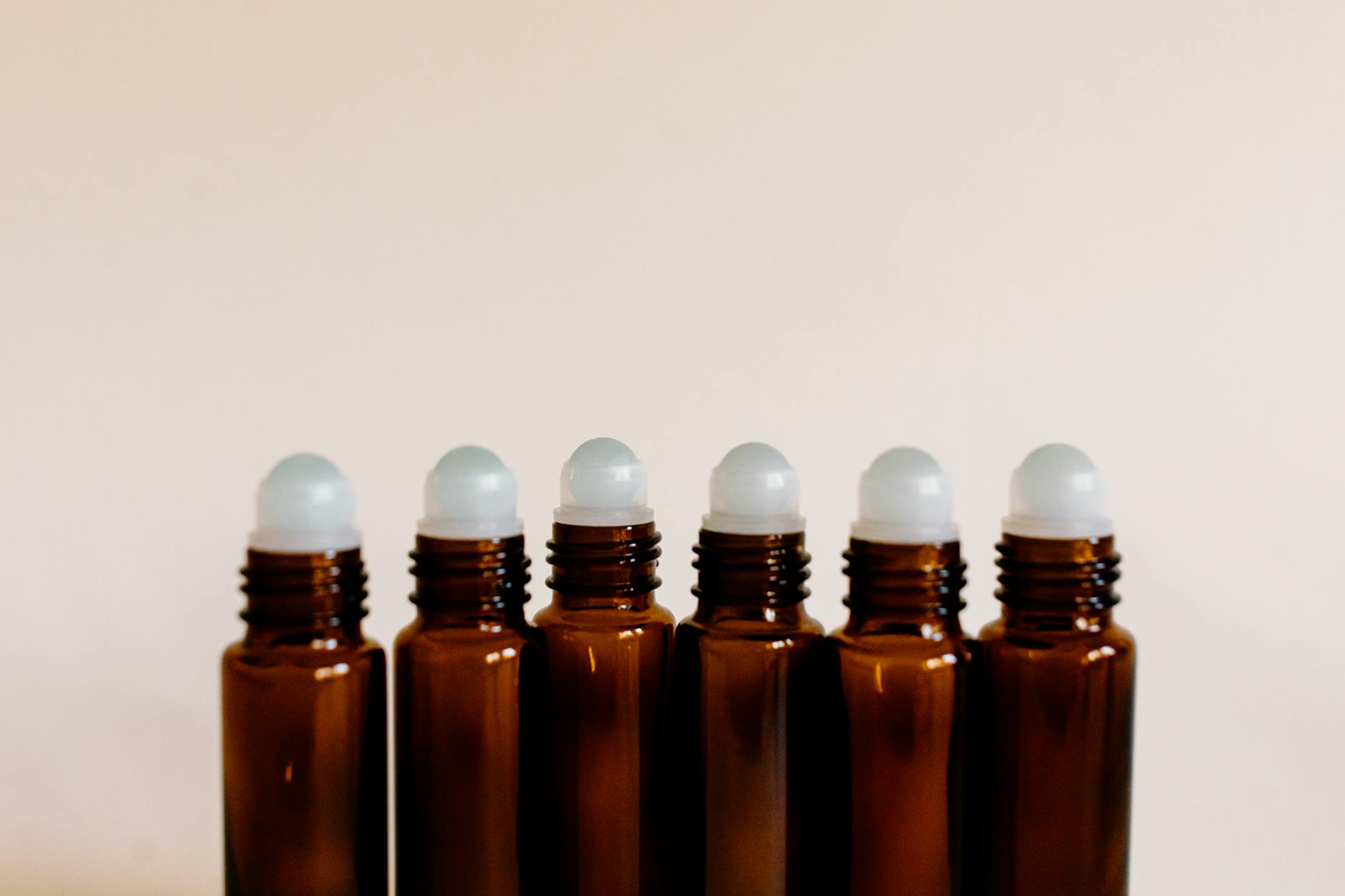 Ahşap zemin üzerinde damlalıklı bir şişe palmarosa yağı ve yanında taze yeşil palmarosa bitkisi yaprakları.