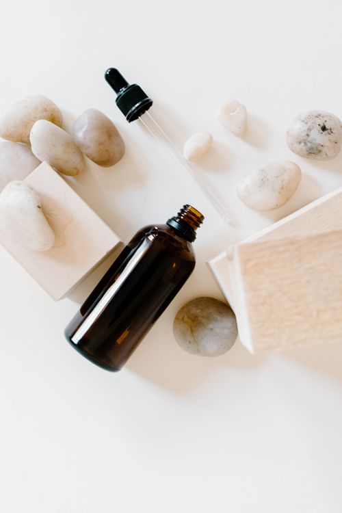 Free Brown essential oil bottle with dropper and stones on clean white background. Perfect for spa and wellness themes. Stock Photo
