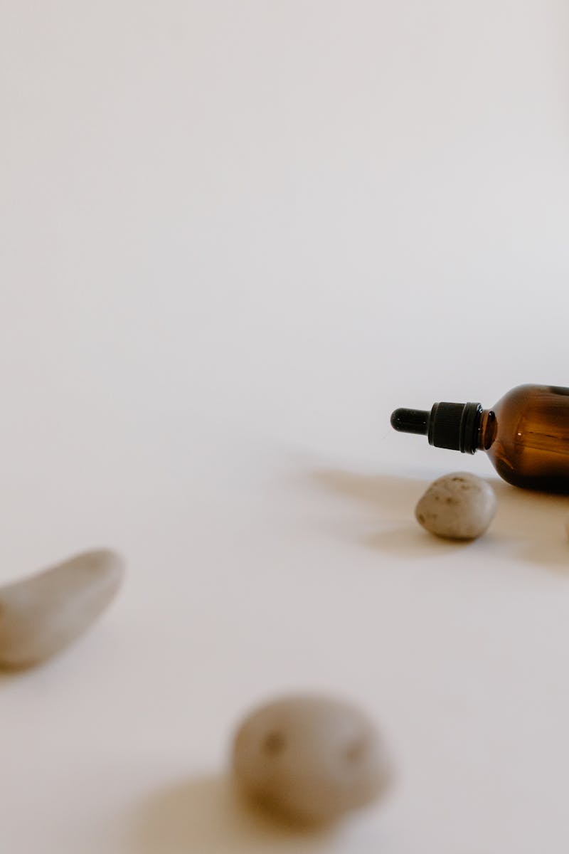 Brown essential oil dropper bottle on a minimalist background with stones, ideal for wellness themes.
