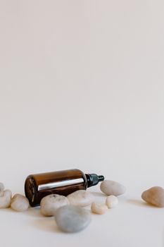 Brown essential oil bottle on a white surface surrounded by smooth stones for aromatherapy.