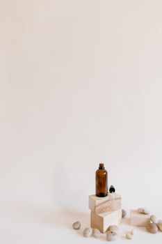 Aromatherapy brown bottle with dropper on wooden blocks surrounded by stones against a white background.