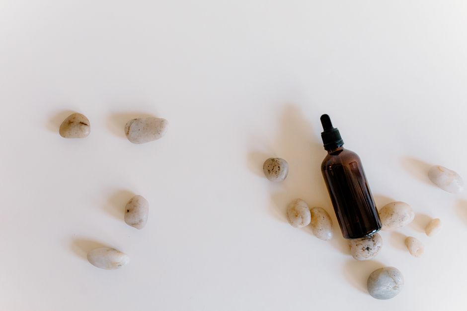 A brown essential oil bottle surrounded by white stones on a white surface, perfect for wellness themes.