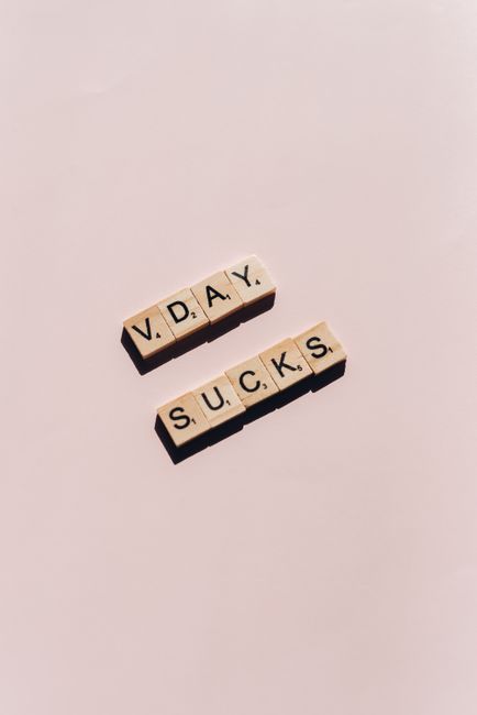 Fotomural Letras de Scrabble sobre un fondo beige que dicen 'V.DAY SUCKS', transmitiendo un tema anti-Día de San Valentín.